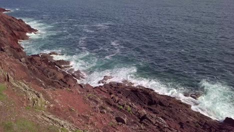 Drone-footage-of-the-sea-with-crashing-waves-against-the-red-colored-cliffs