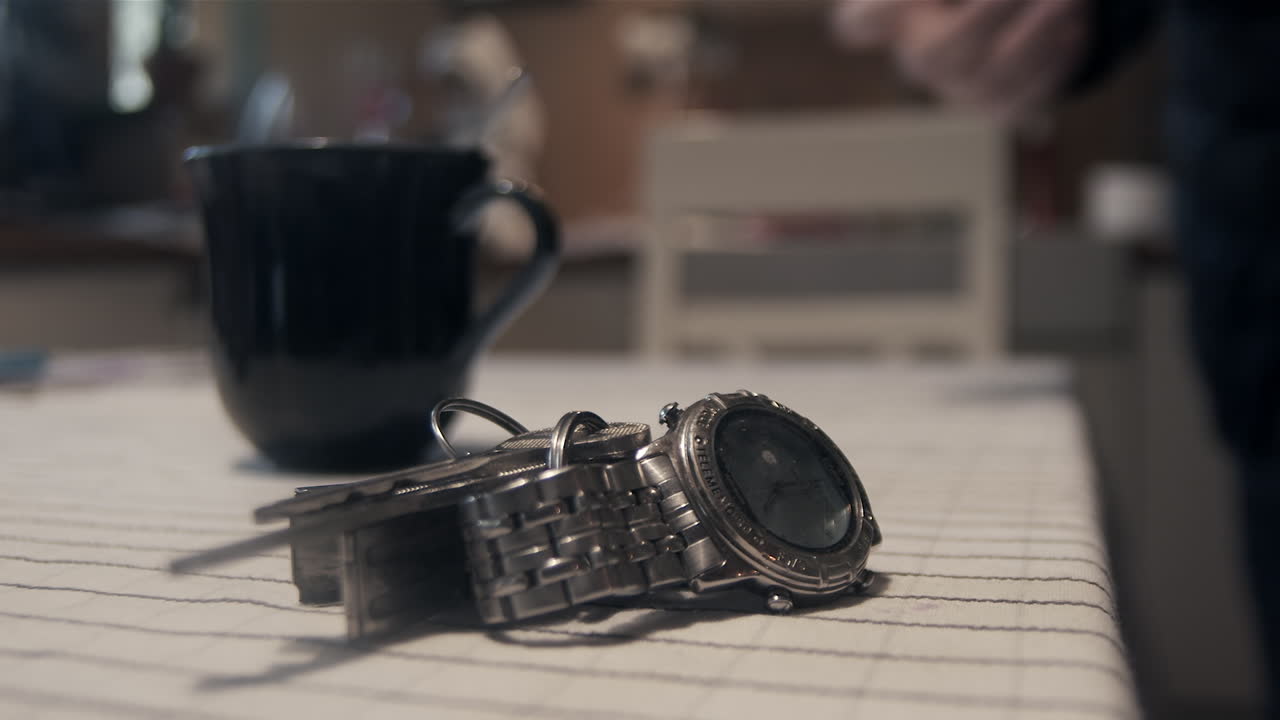 Un homme enfile son manteau, boit du café et prend sa montre et ses clés au premier plan, dans la précipitation matinale, gros plan