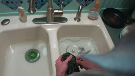 cleaning a fork in the sink doing the dishes and handing the fork to a helper who dries off the fork