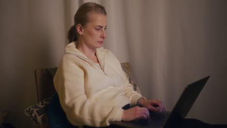 close-up of a woman working at night against the background of a fireplace on a laptop and writing an email