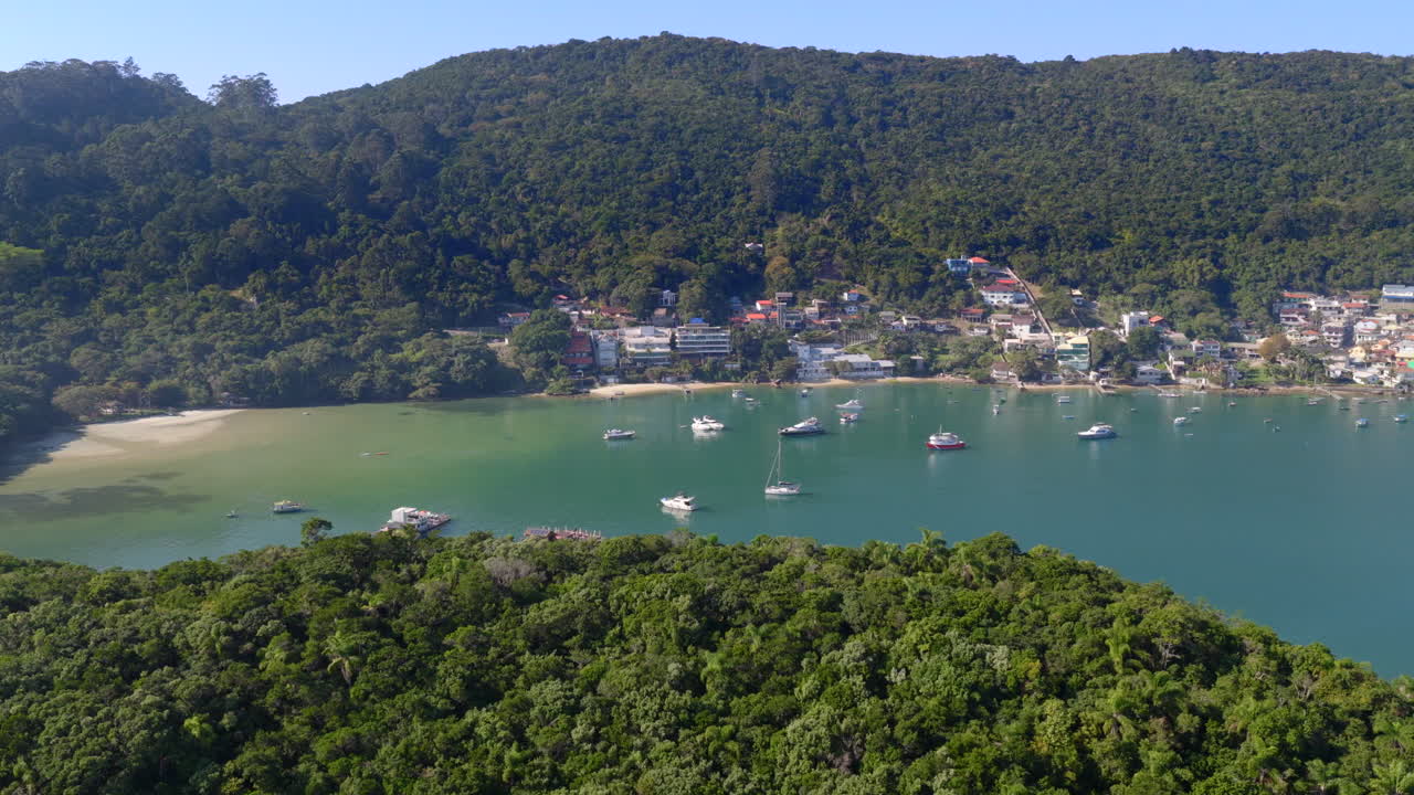Imagem de drone de um caminhão à direita sobre a Praia de Caixa D’aço, barcos e colinas exuberantes em Porto Belo, Brasil