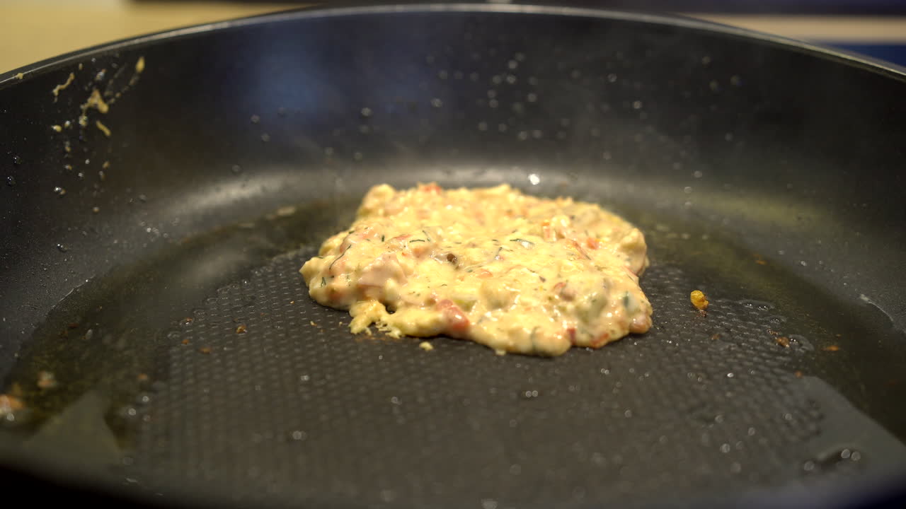 큰 검은색 플라스틱 숟가락으로 완전 채식 팬케이크의 재료를 핫 플레이트에 올려놓습니다.