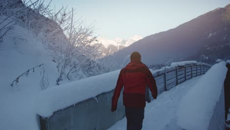 fixed shot, person frome side in hiking clothes walking across snow covered bridge