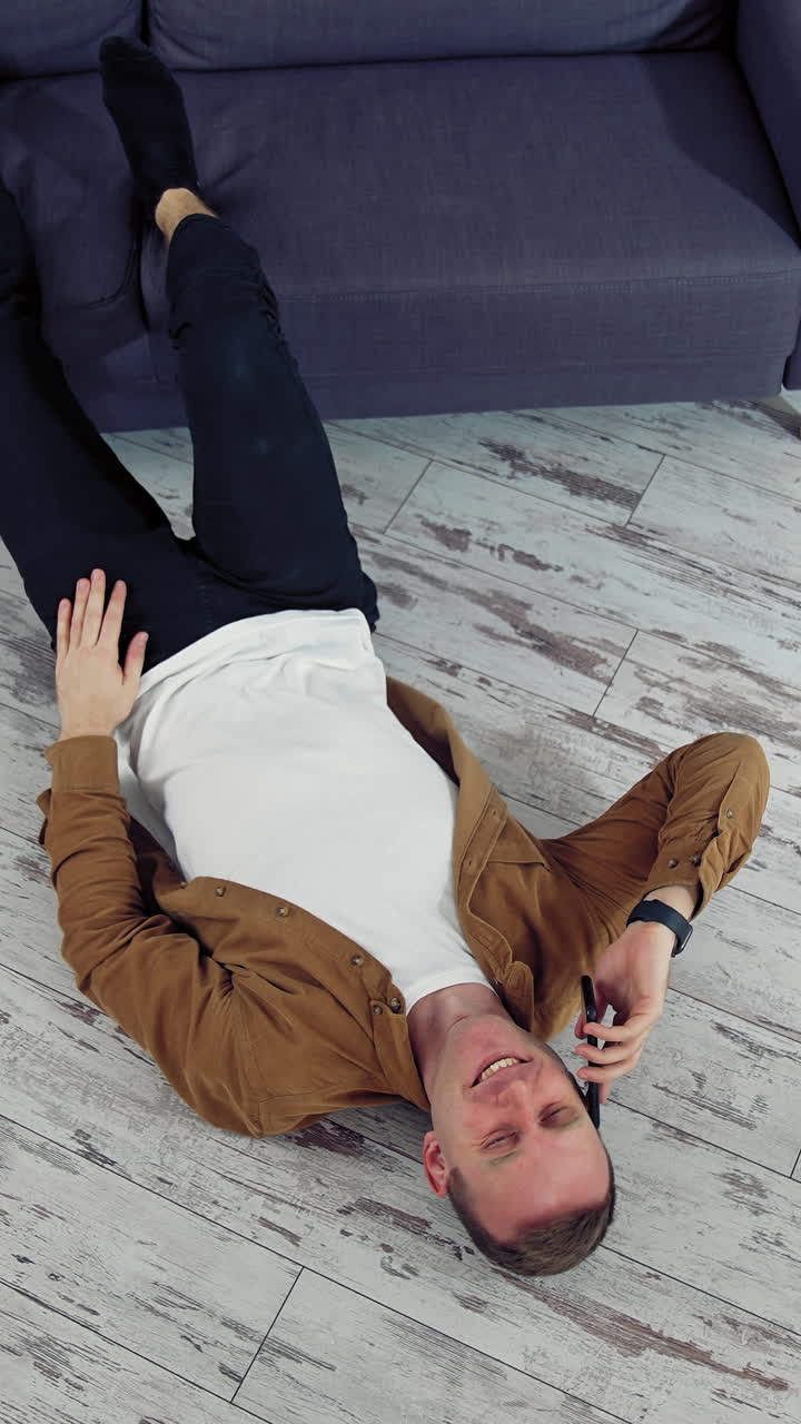 Man relaxing using mobile phone. Happy young man talking on mobile phone and lying on the floor