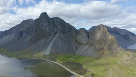 steep black mountain with road over lagoon, blue cloudy sky, aerial