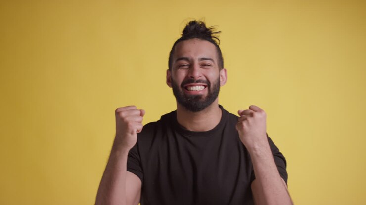 Ritratto in studio di giovane uomo che festeggia buone notizie in piedi su sfondo giallo