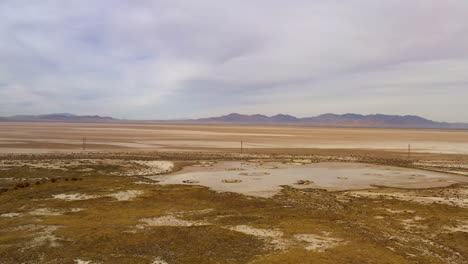 Arid-landscape-of-ancient-lake-bed-in-Arizona-with-electric-pylons,-drone-forward