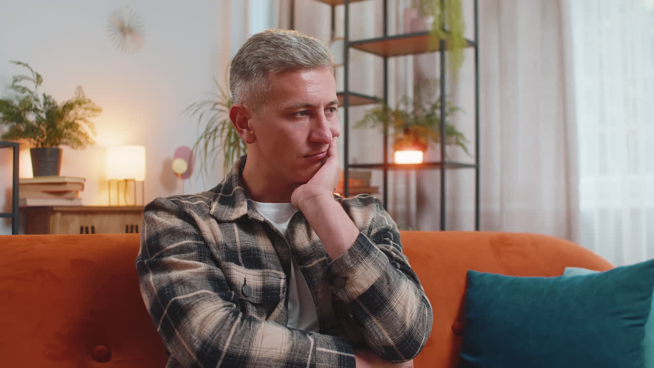Thoughtful man sitting at home looks pensive thinks of unrequited love depressed bad feeling burnout