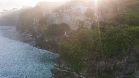 man stands at steep cliff edge overlooking ocean