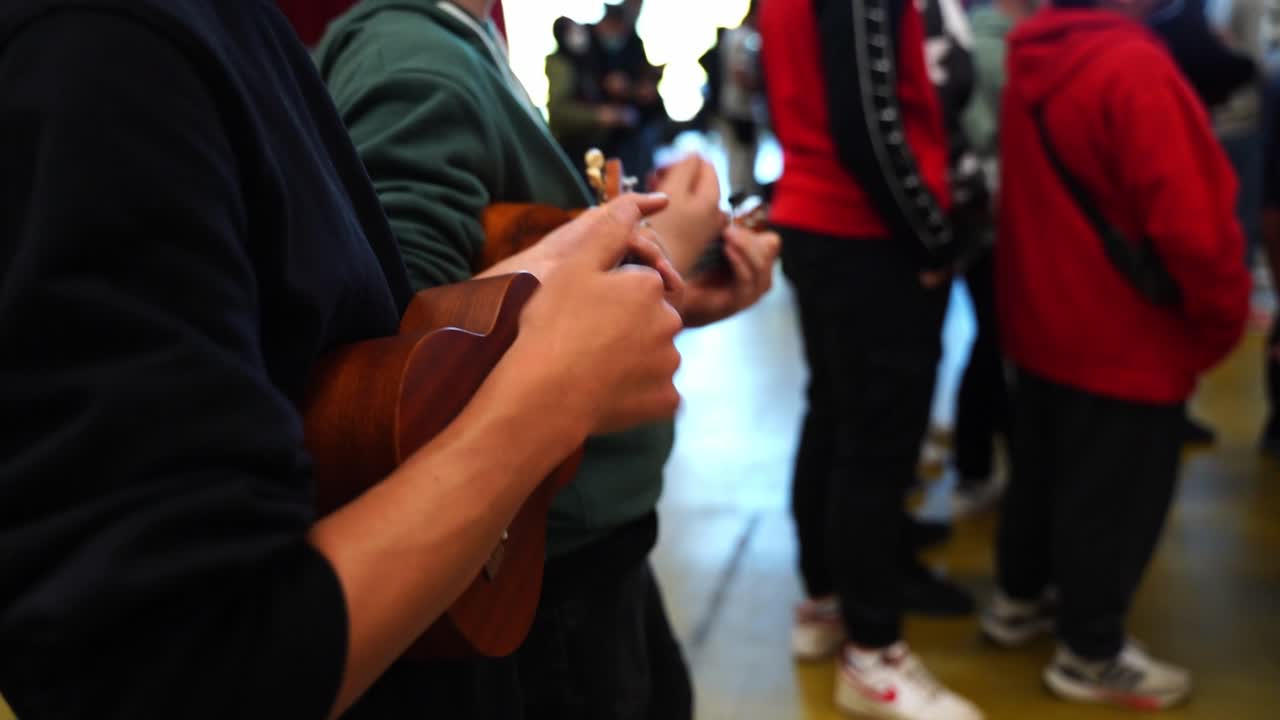 niño en un suéter negro toca acordes simples en un pequeño ukelele