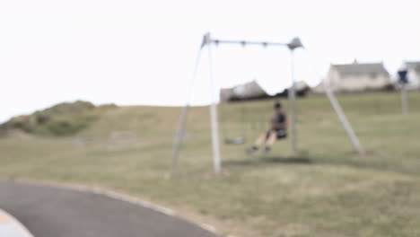 Young-boy-sat-alone-on-a-swing,-blurred-shot,-bored,-possibly-sad