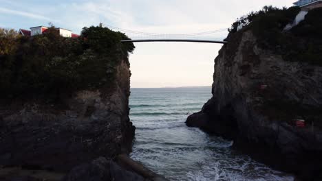 low to high raising aerial shot of bridge connecting a house on an island in the sea on a bright morning at newquay beach, cornwall, uk