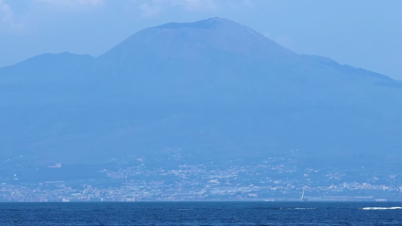 A serene view of Mount Vesuvius with a tranquil sea in the foreground under a clear sky.