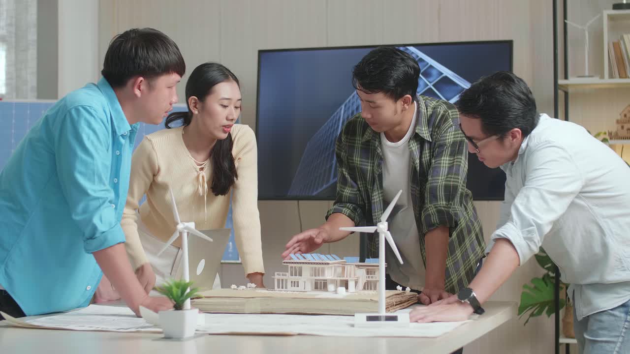 엔지니어링 그룹의 아시아 남성과 여성이 사무실에서 태양 전지판을 가진 작은 집 모델에 대한 회의 중에 논쟁하고 있습니다.