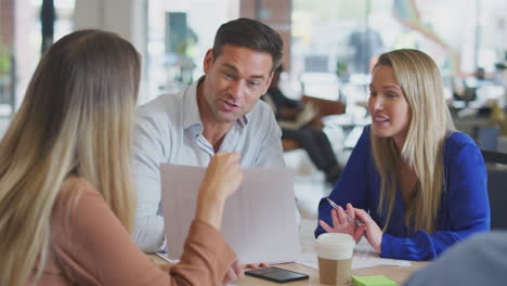 business team having meeting sitting around table discussing document in modern open plan office