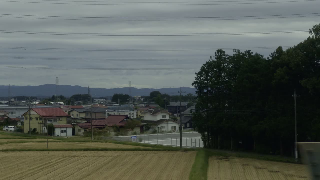 Japanese Countryside Views: Shinkansen Adventure Capture the essence of rural Japan from the Shinkansen, with green mountains, rice fields, and villages set against cloudy weather
