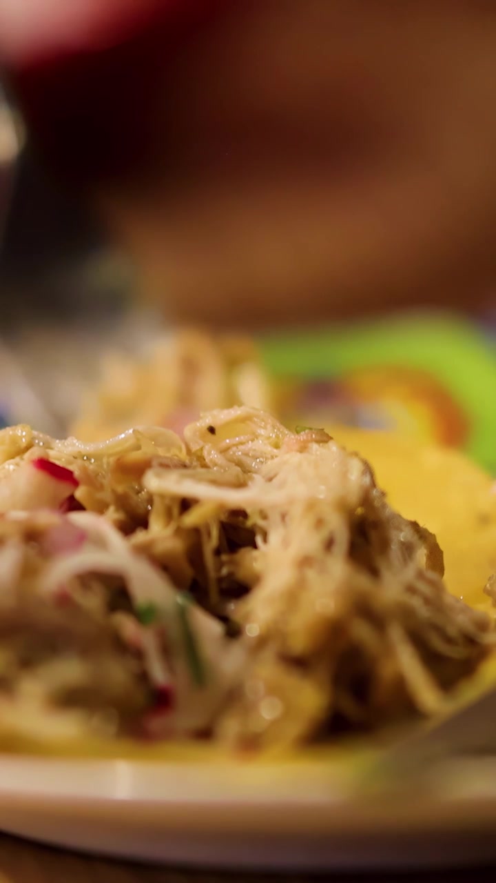 Primo piano di una forchetta che solleva succoso pulled pork sfilacciato su un guscio di taco, con condimenti vivaci, sotto una calda illuminazione interna e una profondità di campo ridotta
