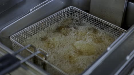 fixed shot of tasty falafel fried in oil in stainless steel basket in restaurant kitchen