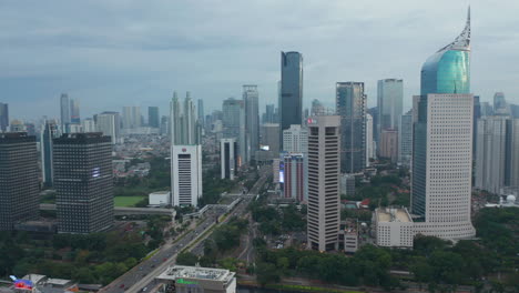 Aerial-pedestal-shot-of-busy-city-traffic-driving-in-the-modern-city-center-with-tall-skyscrapers-in-Jakarta,-Indonesia