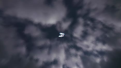 Aerial-top-down-of-couple-wooden-boat-float-on-lake,-cloud-reflection