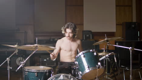 joven baterista masculino sin camisa con barba tocando la batería