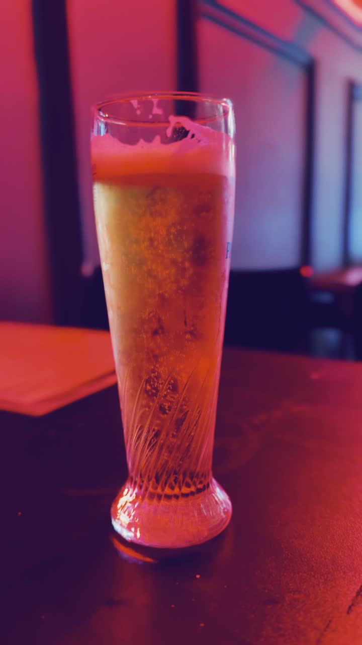 A glass of beer is on a table. The glass is half full and the beer is foamy.