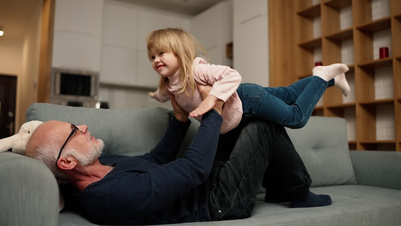 Die Enkelin spielt mit ihrem Großvater auf dem Sofa und tut so, als würde sie fliegen.