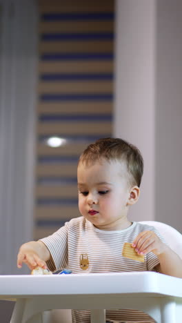 lovely child in high chair picks a cookie and a bun. baby boy choosing food to eat and rises a bun in hand. vertical video