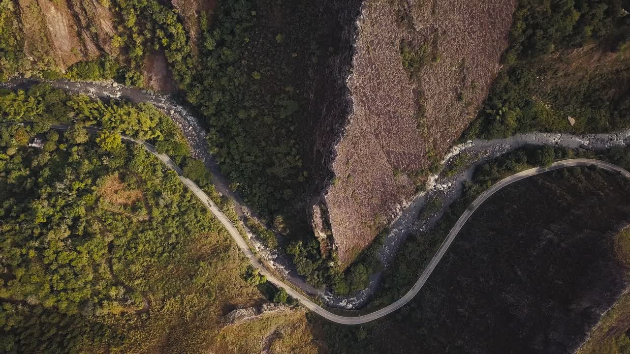 Top-down aerial shot of a Colombian road winding along a river with sharp mountain ridges in a sunny afternoon.