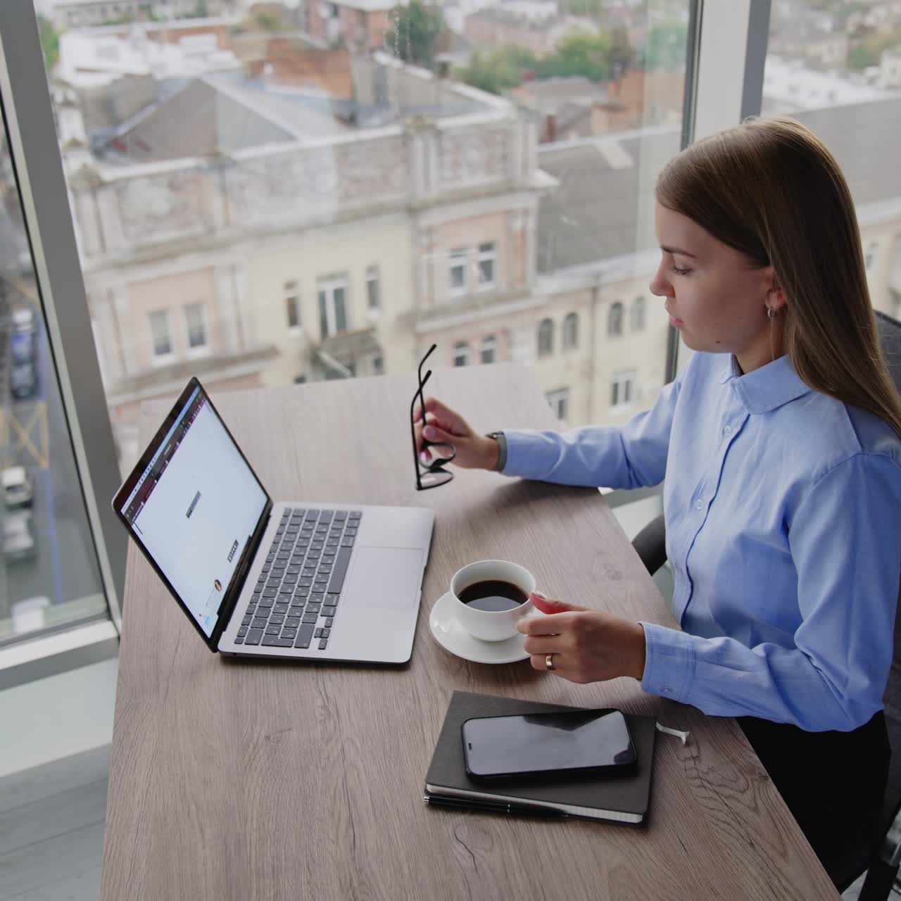 Giovane donna bionda impegnata al lavoro in ufficio durante una pausa. Donna seduta di fronte al laptop con una tazza di caffè. Ripresa dall'alto