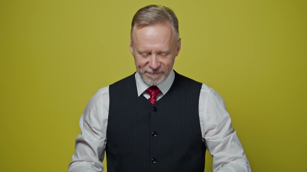 Portrait of a handsome grey-haired man. Mature man taking off his eyeglasses with a smile and looking at camera on yellow background.