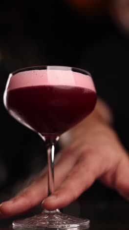 close up of a pink cocktail being held by a bartender