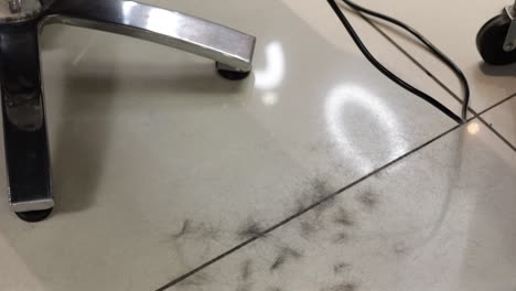 a imagem mostra cortes de cabelo escuro caindo no chão do salão durante um corte de cabelo