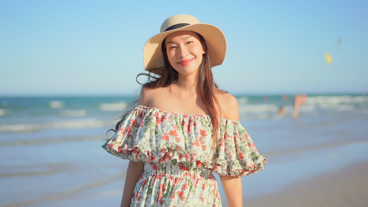 Asian millennial woman with hat on a beach smiling at the camera