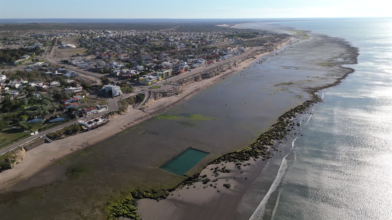 A wide-angle view of Las Grutas beach with the coastline stretching into the distance. The clear waters, sandy beach, and coastal cliffs offer a beautiful contrast.