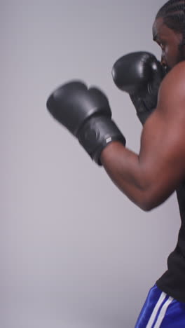 tomada de estudio de video vertical de un boxeador masculino luchando con un entrenador que usa guantes o guantes de puñetazos practicando para la pelea