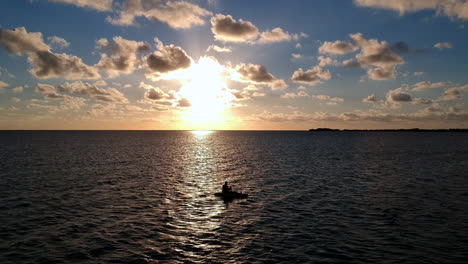 silhouette of person kayaking in the ocean during sunset, static aerial