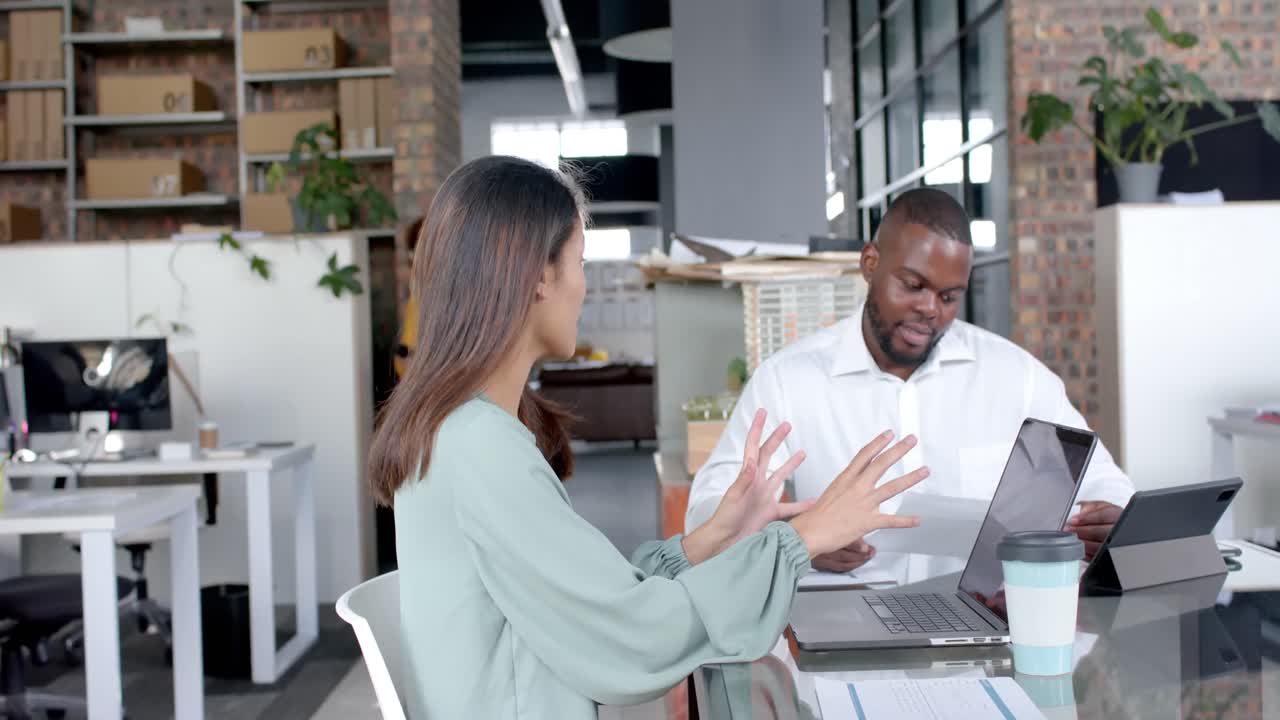Happy diverse colleagues using laptop and tablet discussing in casual meeting at office, slow motion