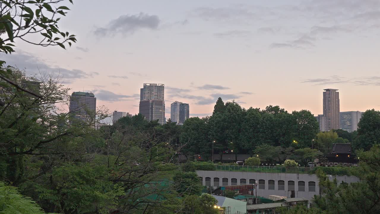 A serene elevated view of Yotsuya, Tokyo, at dusk, showcasing a lush green landscape with distant modern buildings and a softening sky.