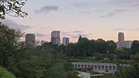 a serene elevated view of yotsuya, tokyo, at dusk, showcasing a lush green landscape with distant modern buildings and a softening sky.