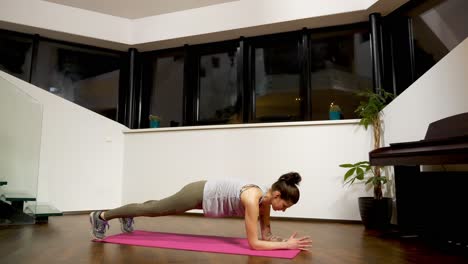 mujer haciendo ejercicio de tabla en la alfombra en casa, entrenamiento interior por la noche, enfoque en la salud
