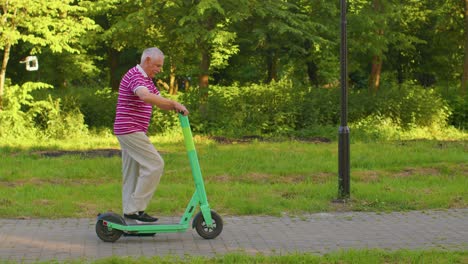 Älterer,-Stilvoller-Großvater-Fährt-Elektroroller-Im-Park,-Moderner-Opa-Fährt-Stadtfahrzeug