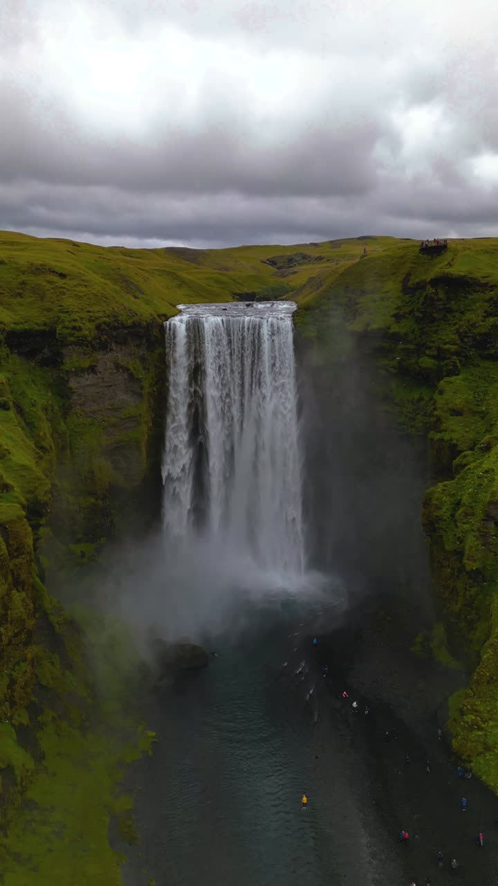 4K cinematic drone footage of Skógafoss Waterfall in Iceland, capturing the immense curtain of water cascading from towering cliffs surrounded by lush green landscapes. Iceland_13