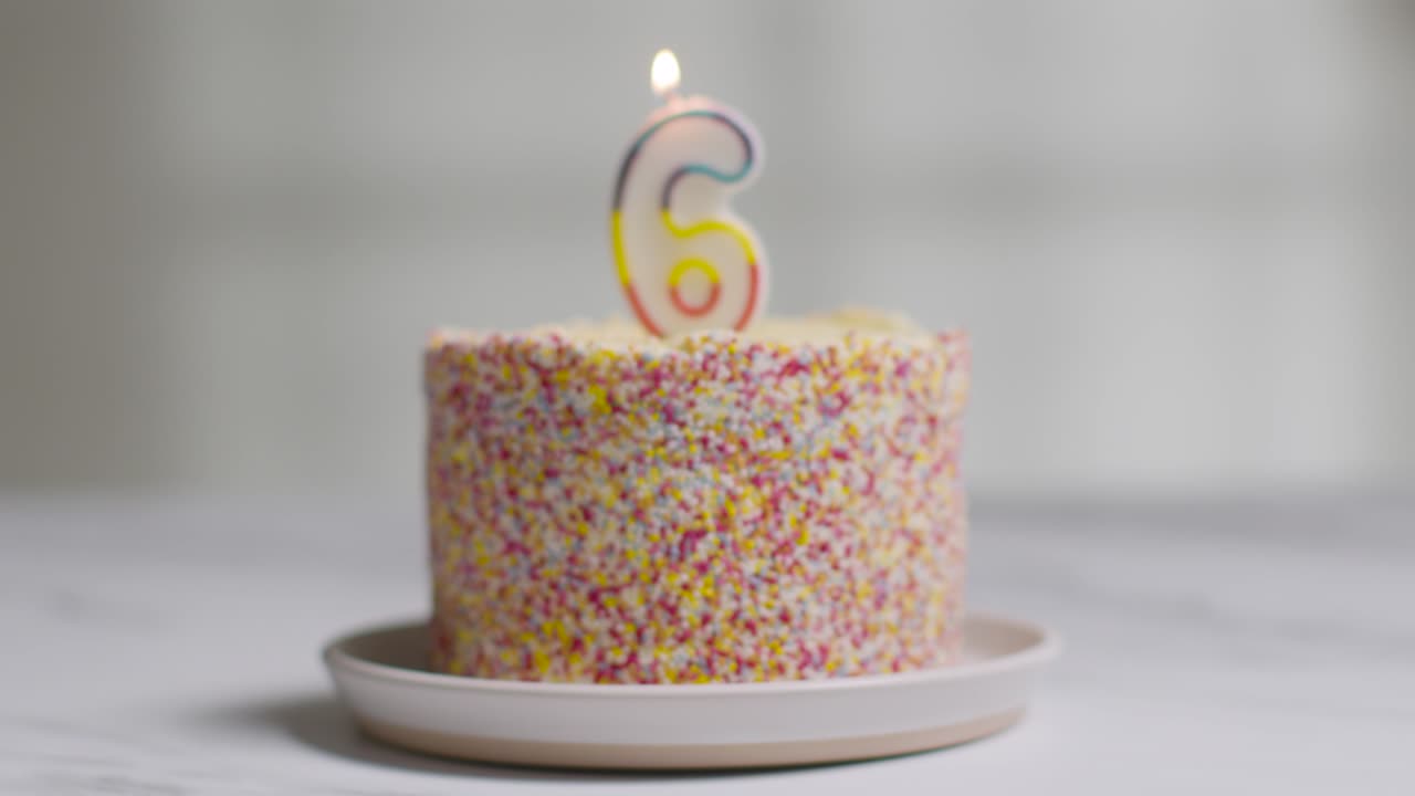 foto de estudio pastel de cumpleaños cubierto con decoraciones y velas encendidas celebrando el sexto cumpleaños que se apaga