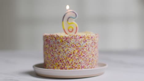 studio shot birthday cake covered with decorations and lit candle celebrating sixth birthday being blown out