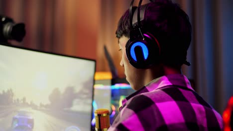 close up back view of asian boy streamer screaming goal and dancing celebrating winning car racing game on personal computer.  live stream video game, desk illuminated by rgb led strip light