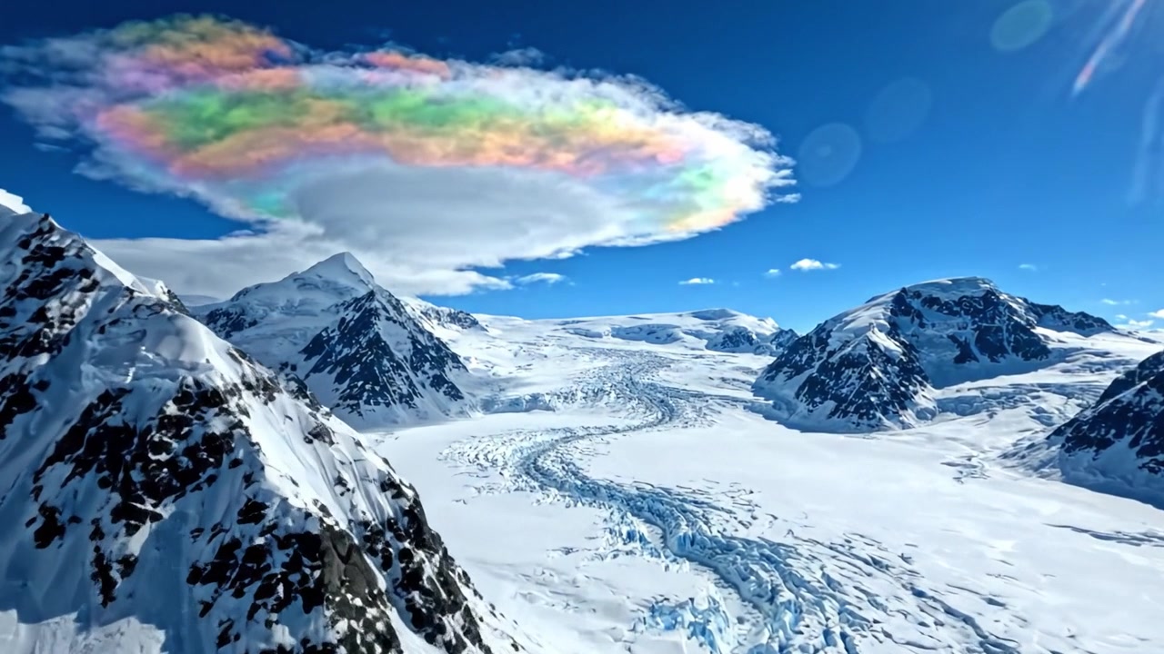 Adembenemend luchtbeeld van een kleurrijke lenswolk boven besneeuwde bergen en een gletsjer, dat de majestueuze schoonheid van een winterlandschap vastlegt.