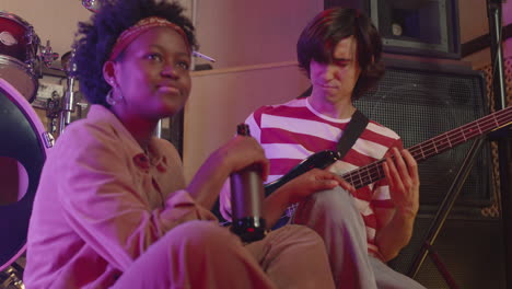 energetic boy playing guitar while girl listening to him and drinking beer during a rehearsal in recording studio