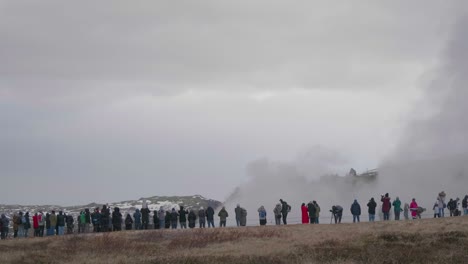 estático, plano general, de mucha gente mirando el geisir en erupción, en un día nublado, lluvioso, de otoño, en geysir, islandia