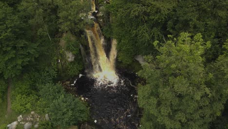 Rising-drone-shot-of-rare-powerful-Yorkshire-Waterfall-within-a-surrounding-of-trees-in-autumn